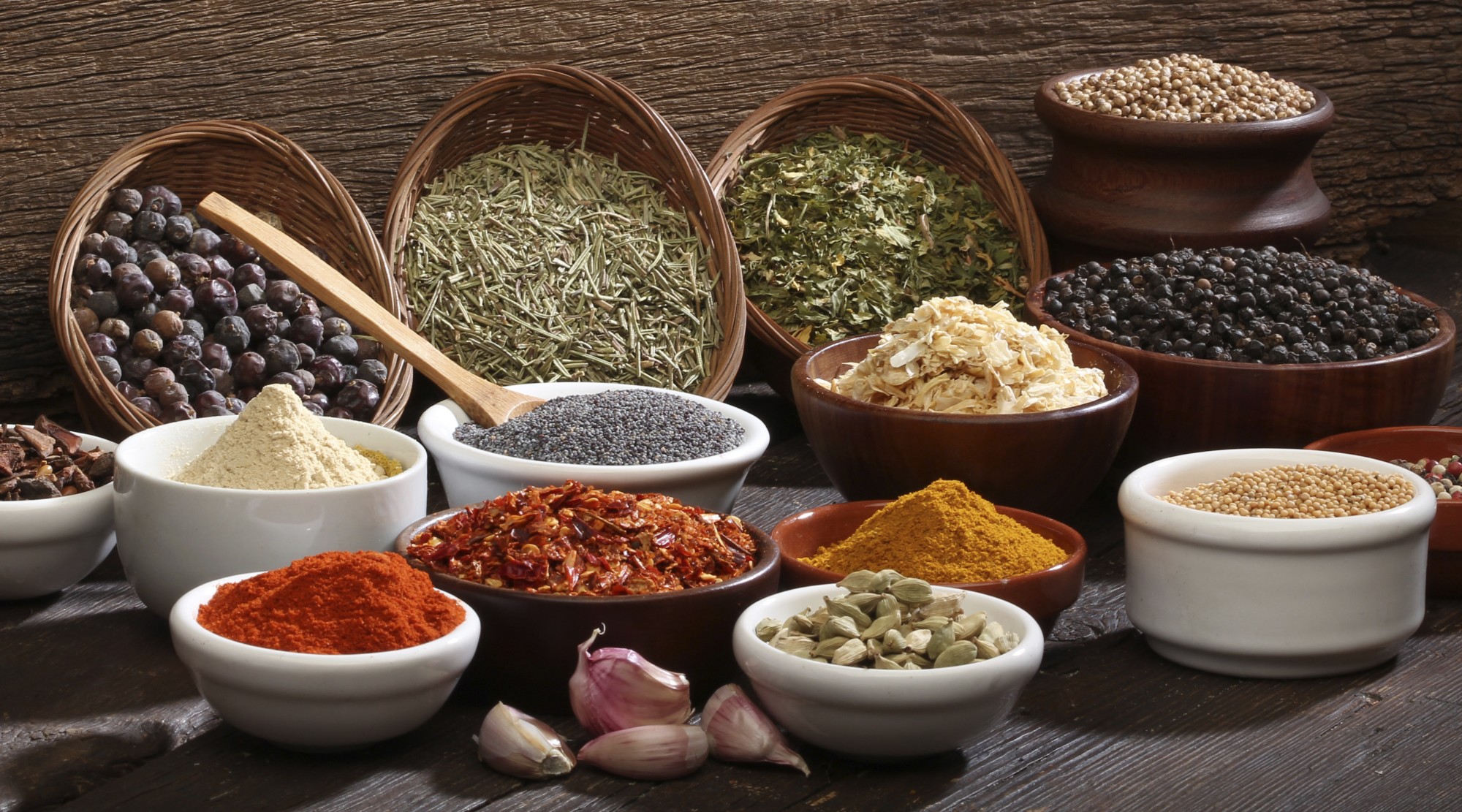 Bowls of whole and ground spices, dried herbs, chiles, cardamom, and peppercorns on a wooden table